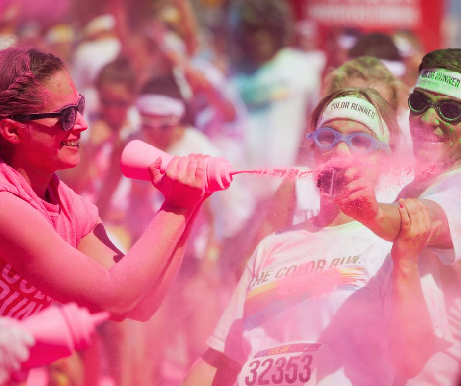 Someone being thrown pink colour powder at her with a squeezing bottle while doing a colour run