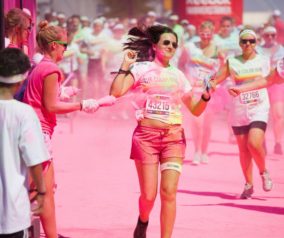 Someone being thrown pink colour powder at her with a squeezing bottle while doing a colour run